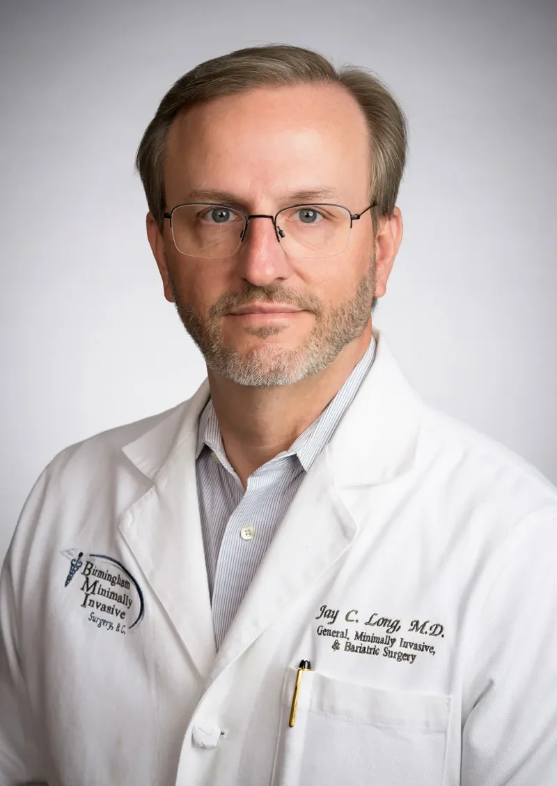 Male doctor headshot in white coat and glasses, professional medical portrait with clinic logo.
