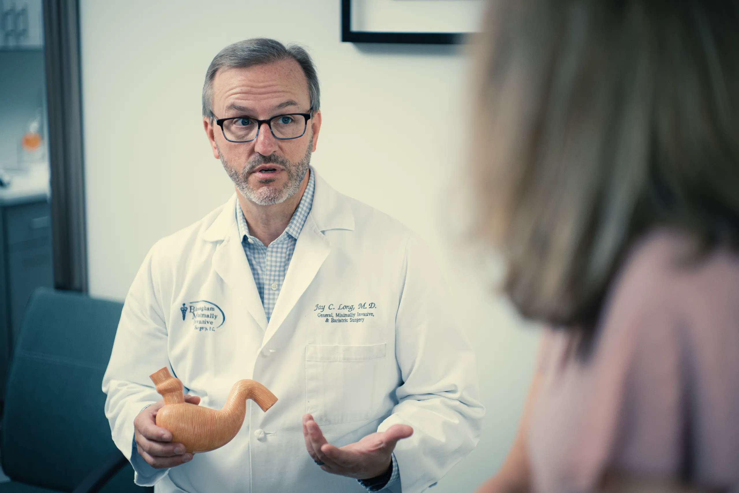 A male bariatric surgeon in white coat holding wooden stomach model during patient consultation