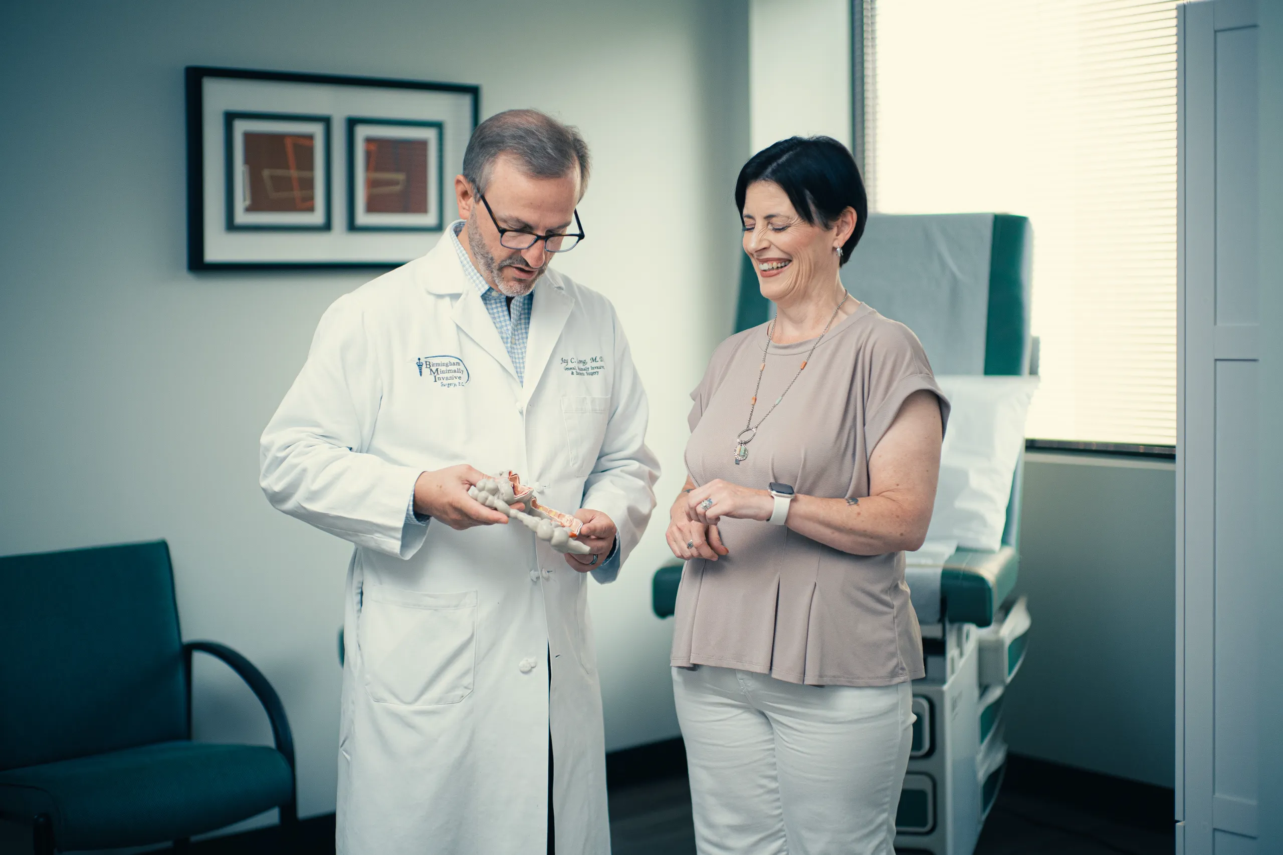 Doctor showing spinal model to a smiling woman during consultation in a modern medical exam room
