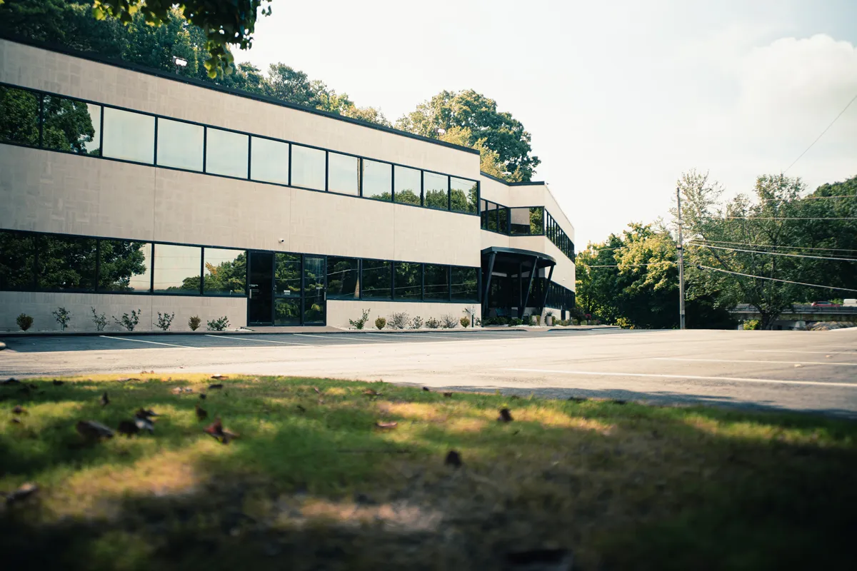 Modern two-story office building with large reflective windows, empty parking lot and landscaped trees on a sunny day
