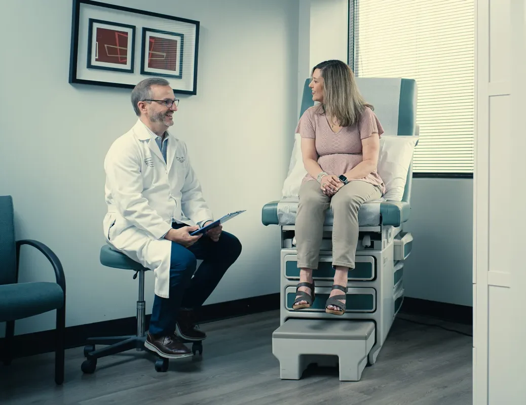 Doctor consulting with a woman on an exam table in a bright medical office, both smiling during appointment.