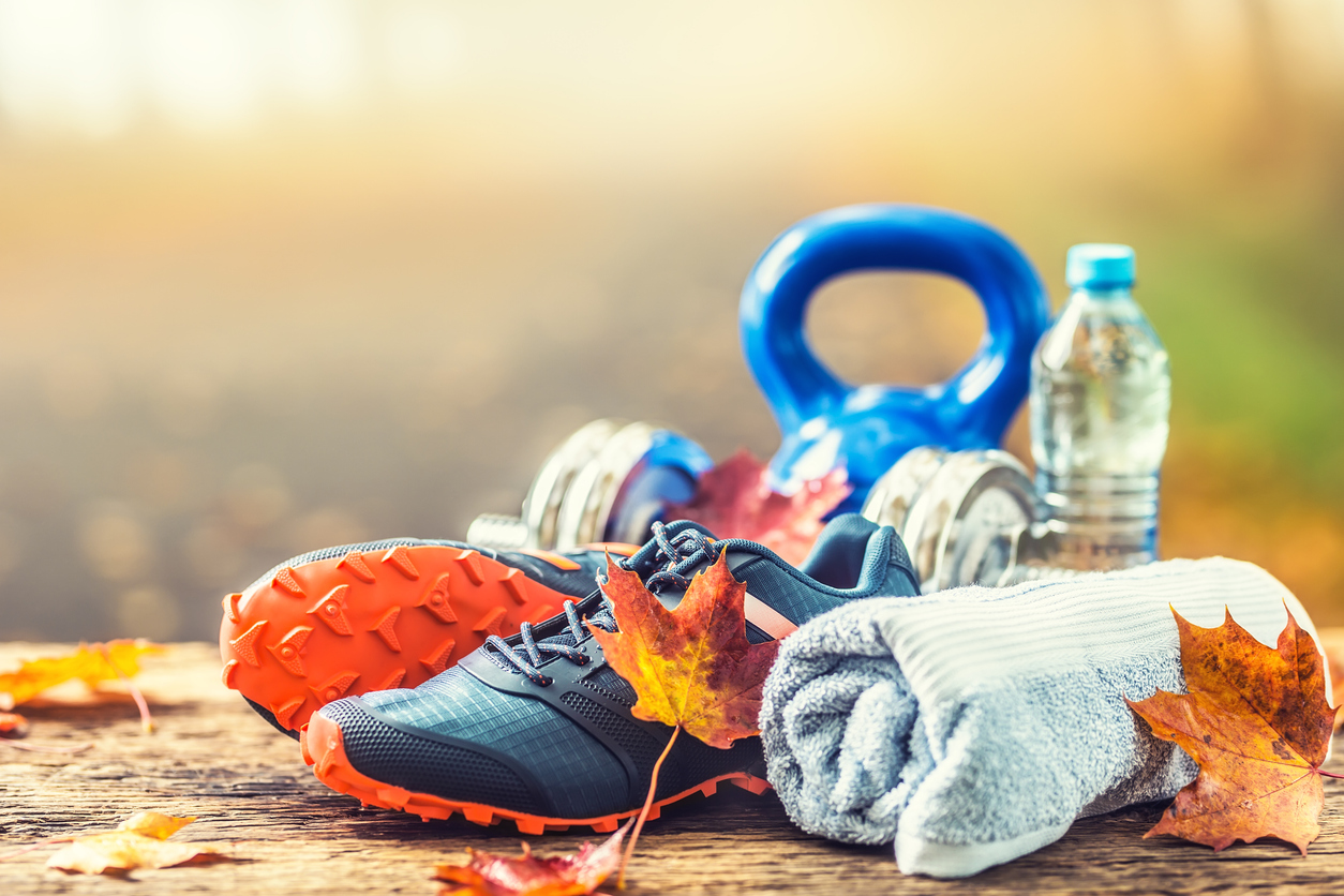 Tennis shoes, a water bottle, and a kettlebell surrounded by falling autumn leaves representing weight loss during colder months.