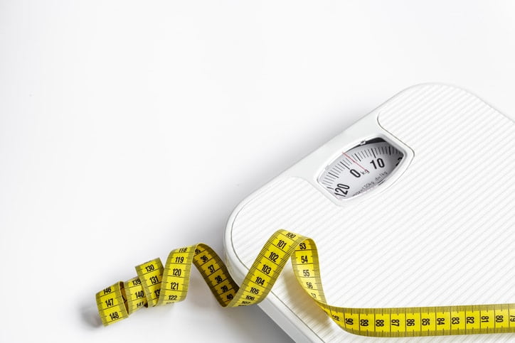 A white scale and a yellow measuring tape on a plain background.
